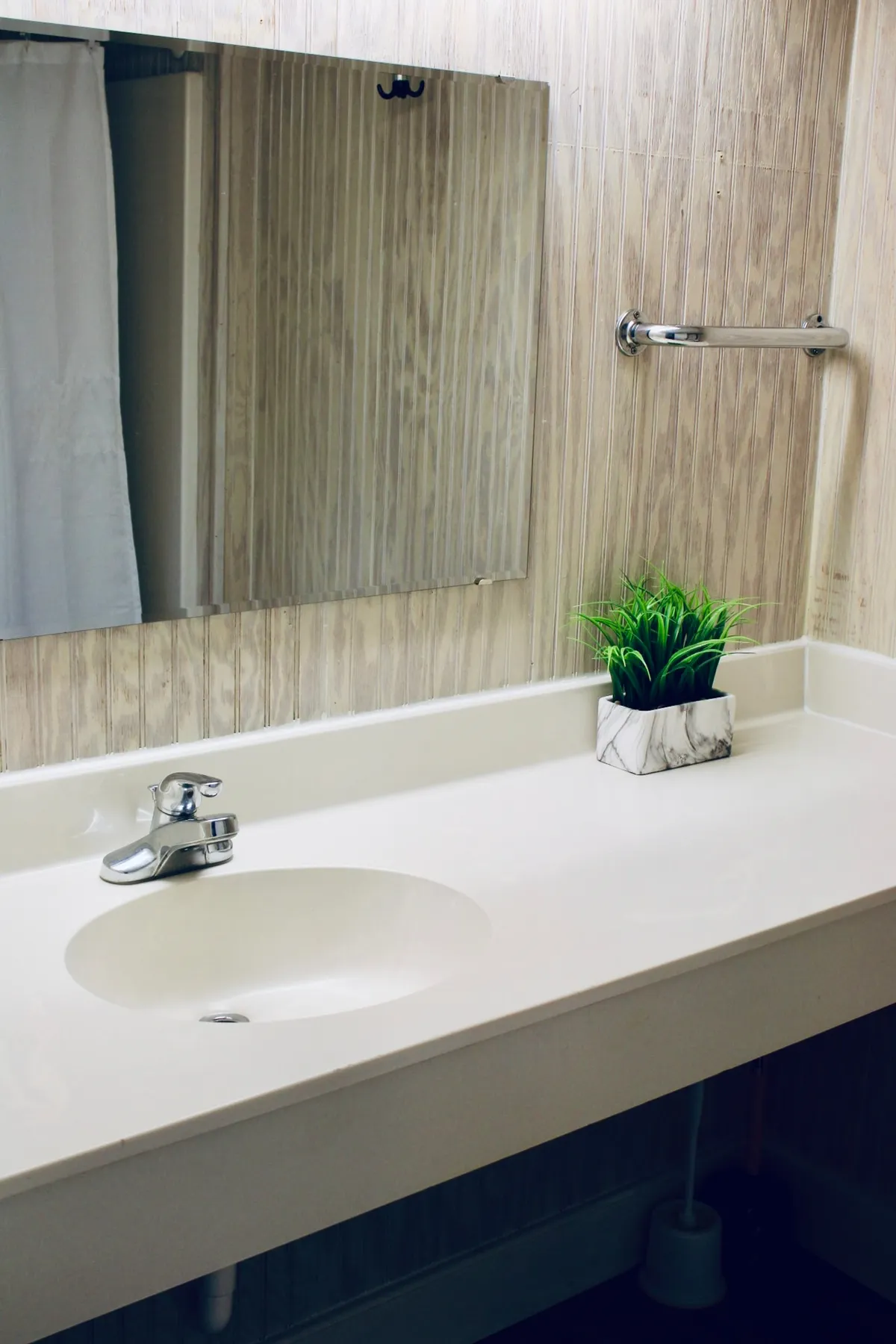 A clean and modern interior space with a stylish sink, large circular mirror, and a vibrant potted plant. The setup suggests a fresh and effortless routine, ideal for quick morning rituals in a compact environment.