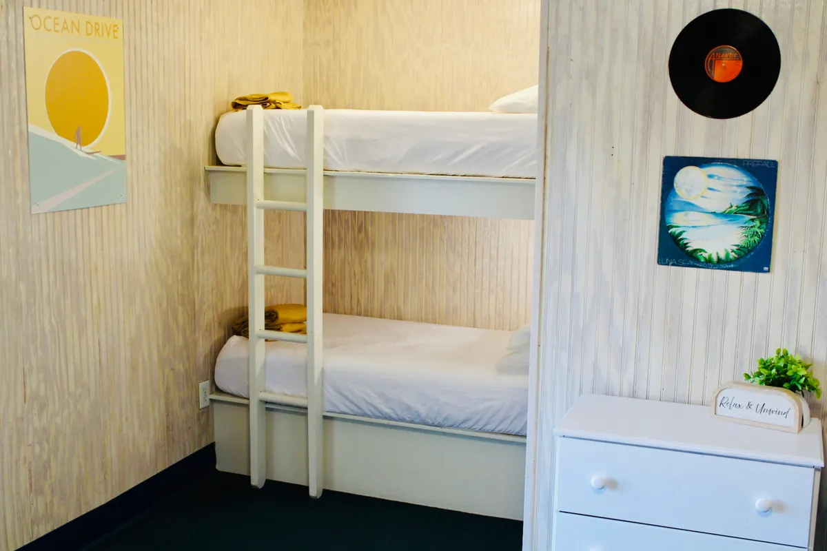 This image presents a cozy interior with playful bunk beds, ocean-themed artwork, a vinyl record, and a small dresser. The light and relaxed atmosphere suggests a comfortable retreat after an adventurous day outdoors, echoing the spirit of rest and togetherness.