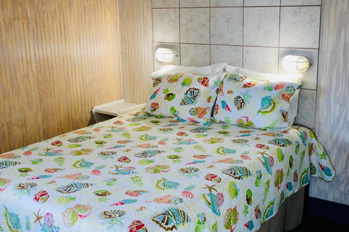 This image features a bright and inviting sleeping area with a bed adorned with a colorful quilt, a nightstand, and wall sconces. The bedding looks plush and the overall decor is cheerful, contributing to a cozy and welcoming atmosphere ideal for rest and relaxation.